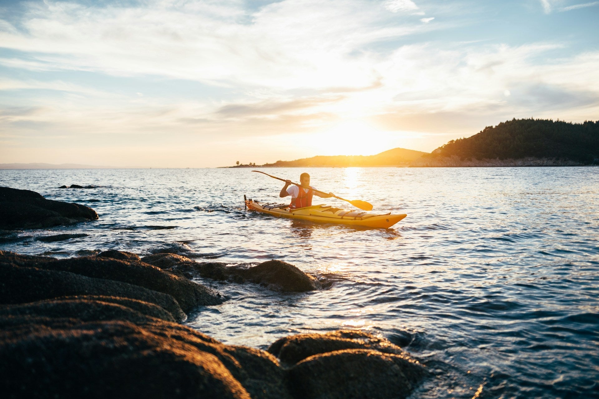wide shot of a man ocean kayaking during sunset